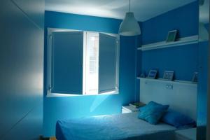 Dormitorio azul con cama y ventana en Piso en Santa Cristina, a 150 m de la playa, en Oleiros