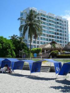 eine Gruppe blauer Sonnenschirme an einem Strand mit einem Gebäude in der Unterkunft Costazul Suites 705 in Santa Marta