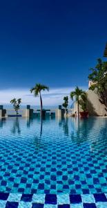 a blue swimming pool with palm trees and the ocean at Mui Ne Hills Backpackers in Mui Ne