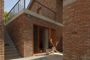 a woman sitting on a bench in front of a brick building at Sansa Village Boutique Hotel at Mutianyu Great Wall in Huairou