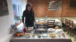Pension Waldegg - restaurant في ساس-الماغيل: امرأة تقف أمام طاولة مع الطعام