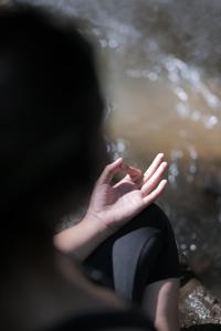 eine Person, die auf einem Stein mit den Händen im Wasser sitzt in der Unterkunft Pramana Giri Kusuma in Payangan