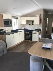 a kitchen with white cabinets and a wooden table at Stunning deluxe 3 bedroomed caravan with CH, DG and decking. in Blackpool