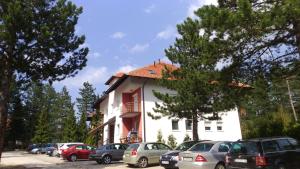 ein weißes Gebäude mit Autos auf einem Parkplatz in der Unterkunft Apartman Happy in Zlatibor