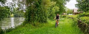 a woman riding a bike down a path next to a river at Camping de l'Hippodrome in Sablé-sur-Sarthe