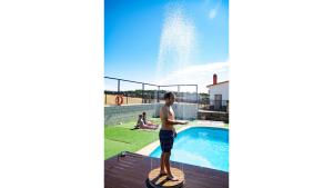 a boy standing on a paddle board next to a swimming pool at Apartamentos Rurales Monfragüe in Torrejón el Rubio