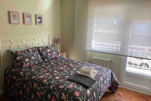 1 dormitorio con 1 cama con colcha de flores y ventana en Coqueto apartamento cerca de la playa, en Santander
