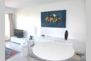 a white living room with a white table and a tv at F2 Climatisé Piscine Proche Plage in Cavalaire-sur-Mer