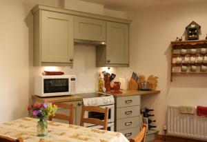 eine Küche mit grünen Schränken und einem Tisch mit Blumen in der Unterkunft Drumena Cottage in Kilcoo