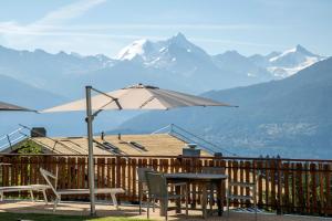 einen Tisch, Stühle und einen Regenschirm auf einer Terrasse mit Bergen in der Unterkunft Hotel Ad'Eldorado in Crans-Montana