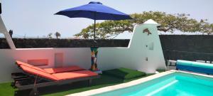 un patio con una silla y una sombrilla junto a la piscina en Aptos con piscina clima El Flamboyán 1, en Teseguite