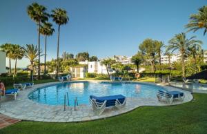 a large swimming pool with chairs and palm trees at Sea View Appartment Miraflores in La Cala de Mijas