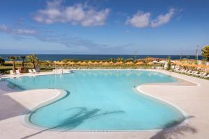 ein großer Pool mit Stühlen und das Meer im Hintergrund in der Unterkunft Barceló Conil Playa - Adults Recommended in Conil de la Frontera