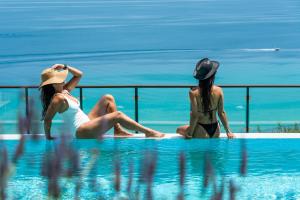 two women sitting on the edge of a swimming pool at Rigas Boutique Hotel & Spa in Afitos