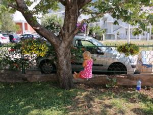 Una bambina seduta su un albero accanto a un'auto di Dom za odmor J&S a Sutomore