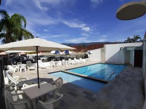 a swimming pool with white chairs and an umbrella at Bella Casa Flat Service in Bertioga