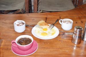 a table with two cups of coffee and a plate of eggs at Mondi Lodge Kisoro in Kisoro