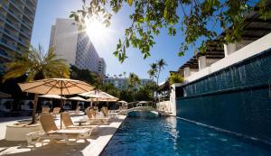 una piscina con sillas y sombrillas junto a un edificio en Emporio Acapulco, en Acapulco