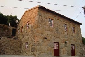 un antiguo edificio de piedra con puertas y ventanas rojas en Casa do Postigo, en Gerês