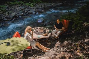 a man and woman sitting around a table next to a river at ЛЕС глэмпинг и спа in Krasnaya Polyana