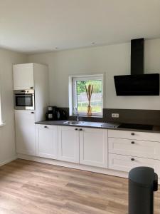 een keuken met witte kasten, een wastafel en een raam bij Zonnehoeve vakantiehuizen in Hollum