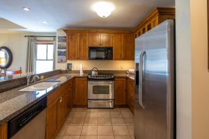 a kitchen with wooden cabinets and a stainless steel refrigerator at Two Bedroom Condo with Balcony over Mountaineer Square - Just Steps from the Slopes! condo in Crested Butte +21 photos