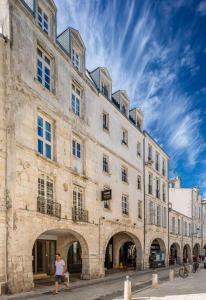 un grand bâtiment en pierre avec deux personnes assises devant dans l'établissement Maisons du Monde Hôtel & Suites - La Rochelle Vieux Port, à La Rochelle