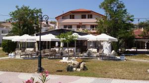 a building with tables and white umbrellas in a park at Verginarooms in Nea Potidaea