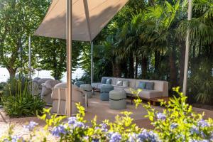 un groupe de canapés et de chaises sous un parasol dans l'établissement Villa Rosa Hotel Desenzano, à Desenzano del Garda