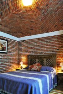 um quarto com uma parede de tijolos e uma cama com lençóis azuis em Casa Geranios Tequisquiapan em Tequisquiapan
