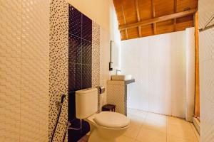 a bathroom with a toilet and a tiled wall at Kelingking Mesari Villa and Spa in Nusa Penida