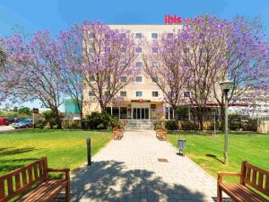 un edificio con dos bancos y árboles con flores púrpuras en Ibis Murcia, en Murcia