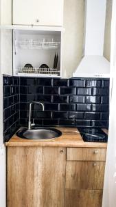 a kitchen with a sink and a black tiled wall at Новая студия на Южном вокзале in Kharkiv