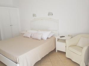 a white bedroom with a bed and a chair at Anixi Hotel in Ornos
