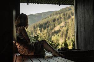 uma mulher sentada no parapeito da janela a olhar para as montanhas em Goldstück - Adults Only em Saalbach-Hinterglemm