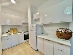 a white kitchen with white cabinets and a basket of flowers at Olive Square Apartment Budva in Budva