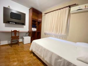 ein Schlafzimmer mit einem weißen Bett und einem Fernseher in der Unterkunft Império Hotel in Caçu