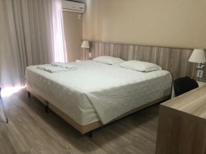 1 dormitorio con 1 cama grande con sábanas y almohadas blancas en Aquarius Flat Aptos e Suítes en Santa Cruz do Sul