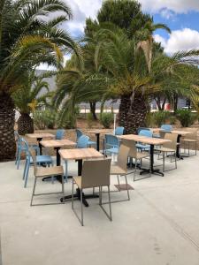 a group of tables and chairs with palm trees at Kyriad Direct Perpignan Nord - Aéroport in Rivesaltes
