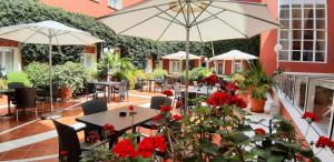 a patio with tables with red flowers and umbrellas at Alborán Chiclana in Chiclana de la Frontera