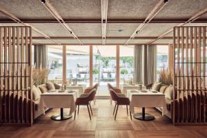 a restaurant with white tables and chairs and large windows at Falkensteiner Hotel Kronplatz - The Leading Hotels of the World in Brunico