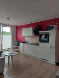 una cocina con armarios blancos y una pared roja en Ferienwohnung ab zum Haff, en Ueckermünde