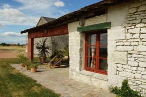 Cette maison en pierre dispose d'une fenêtre rouge et d'une terrasse. dans l'établissement VALINIERE VILLAGE maison détente TENNIS ET PISCINE, à Champigny-sur-Veude