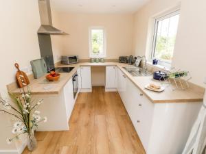 a kitchen with white cabinets and wooden floors at Ramsey Lodge Bier Wood Lodges in Tenby +20 photos