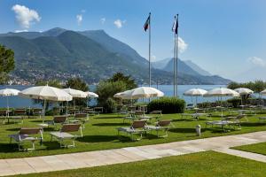 un montón de sillas y sombrillas en la hierba cerca del agua en Park Hotel Casimiro en San Felice del Benaco