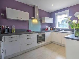 a kitchen with white cabinets and a purple wall at Gîte Herbignac, 4 pièces, 7 personnes - FR-1-306-1105 in Herbignac