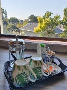 a tray with two tea cups and affeepot on a window at Coral Tree Boutique Guesthouse in East London