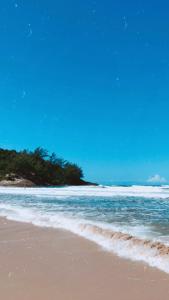 a sandy beach with the ocean and trees in the background at Casinha Astral - Praia da Ferrugem in Garopaba