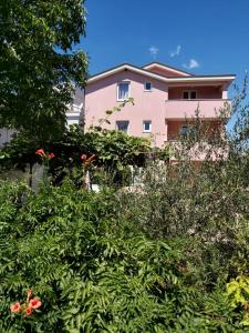 un bâtiment rose derrière des buissons et des arbres dans l'établissement Anđela, à Međugorje