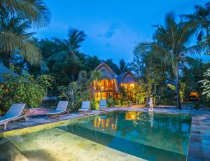 a resort pool with chairs and a house in the background at Sukanusa Luxury Huts in Nusa Lembongan